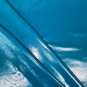 May include: A close-up of a smooth, shiny, teal blue fabric. The fabric is folded and has a slight sheen.