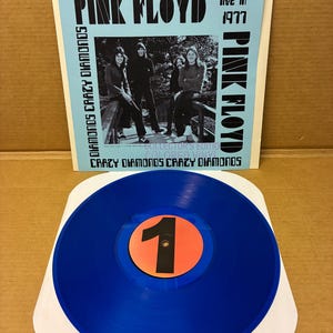 May include: A blue vinyl record with a black number 1 on an orange circle. The album cover features the band Pink Floyd, the text "Pink Floyd live in 1977", and "Diamonds Crazy Diamonds".