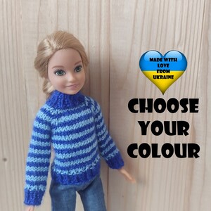 May include: A doll wearing a blue and white striped sweater, blue jeans, and pink shoes. The doll is standing in front of a wooden background. The text "Made with love from Ukraine" is in a heart shape with the Ukrainian flag colors. The text "Choose your colour" is also visible.