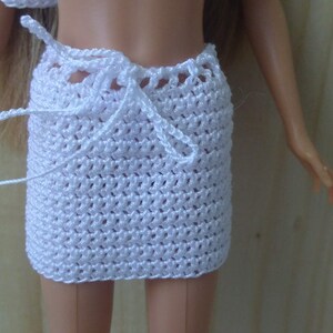 May include: White crocheted skirt with a tie closure. The skirt is made of a fine, delicate yarn and has a simple, elegant design.