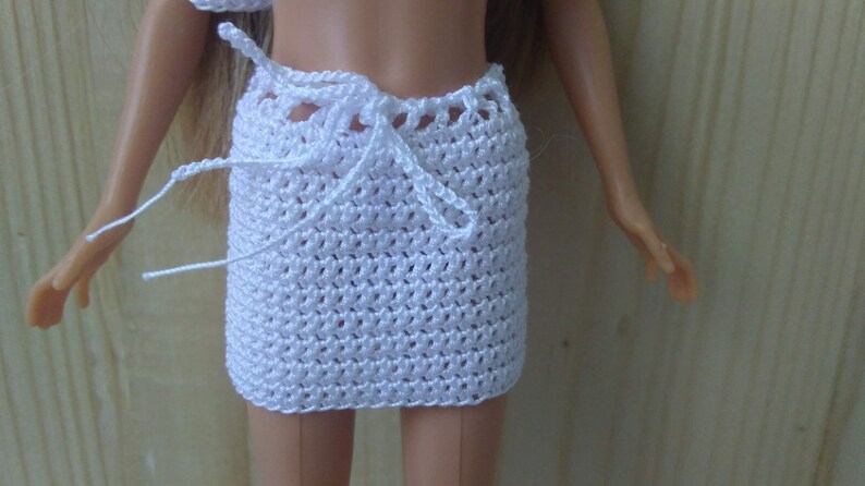 May include: White crocheted skirt with a tie closure. The skirt is made of a fine, delicate yarn and has a simple, elegant design.