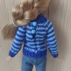 May include: A blue and light blue striped knitted sweater with blue buttons. The sweater is being worn by a doll with blonde hair.