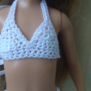 May include: White crocheted bikini top for a doll. The top has a halter style with a triangular shape and a delicate crocheted pattern.