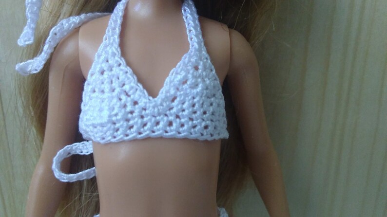 May include: White crocheted bikini top for a doll. The top has a halter style with a triangular shape and a delicate crocheted pattern.