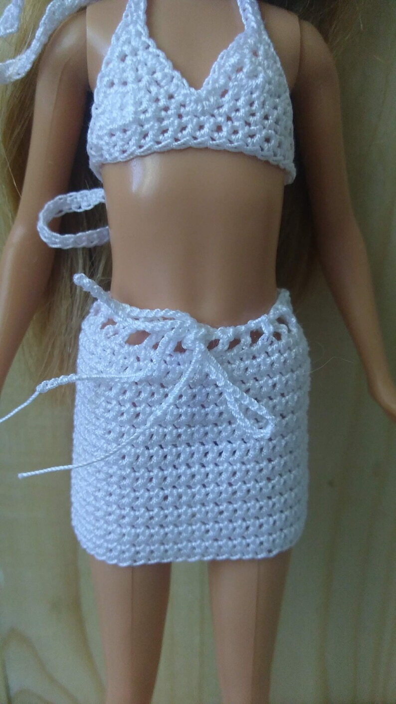 May include: White crocheted bikini top and skirt set for a doll. The top is halter style and the skirt is a wrap style with a tie at the waist.