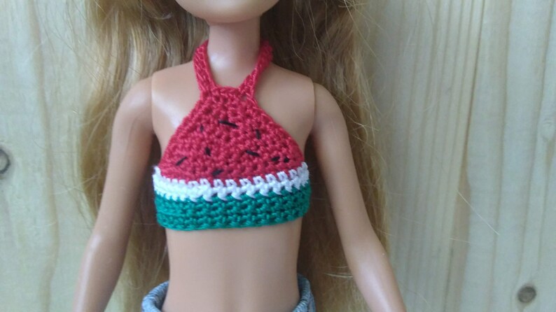 May include: A red, white and green crocheted halter top with a watermelon design. The top is made of yarn and has a halter neck style.
