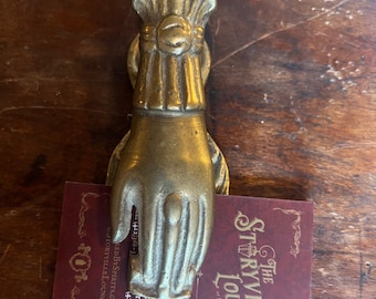 May include: A brass hand-shaped door knocker with a decorative top. The knocker is holding a business card for The Storyville Lounge, located in  Lentown, PA. The card has the address, phone number, and website for the lounge.