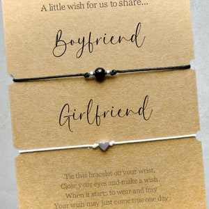 May include: Two friendship bracelets, one black with a black bead and one white with a silver heart charm. The card reads "A little wish for us to share... Boyfriend Girlfriend Tie this bracelet on your wrist, Close your eyes and make a wish. When it starts to wear and fray Your wish may just come true one day."