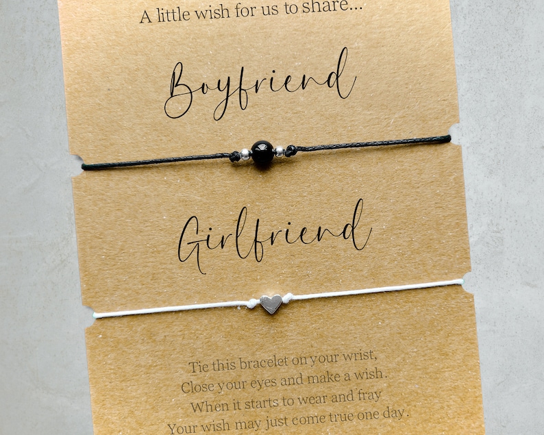 May include: Two friendship bracelets, one black with a black bead and one white with a silver heart charm. The card reads "A little wish for us to share... Boyfriend Girlfriend Tie this bracelet on your wrist, Close your eyes and make a wish. When it starts to wear and fray Your wish may just come true one day."