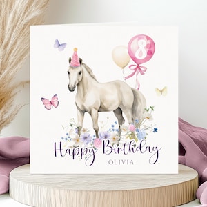 May include: A square greeting card featuring a white horse wearing a pink party hat, surrounded by colourful flowers, butterflies, and balloons. One pink balloon displays the number 8. The text reads Happy Birthday OLIVIA in dark purple script.