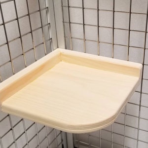 May include: A natural wood corner shelf for a cage. The shelf is rounded on the front edge and has a smooth, unfinished surface.