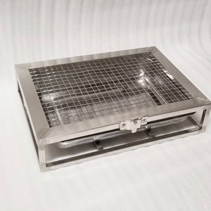 May include: A stainless steel grilling rack with a removable tray. The rack has a hinged lid and a wire mesh bottom.