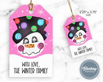 Puede incluir: Etiqueta de regalo rosa con una ilustración de muñeco de nieve. El muñeco de nieve lleva un sombrero negro con lunares de colores, tiene una cara blanca con ojos negros y una nariz de zanahoria, y está sobre un fondo rosa con copos de nieve blancos. El texto de la etiqueta dice "Con amor, La familia de invierno".