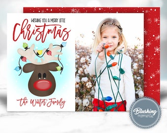 May include: A Christmas card featuring a cartoon reindeer with colorful lights wrapped around its antlers. The text "Wishing you a merry little Christmas" is at the top of the card. The text "The Winter Family" is at the bottom of the card. A photo of a young girl holding Christmas lights is in the background.