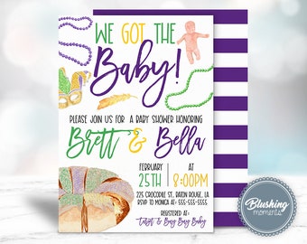 May include: A white baby shower invitation with purple and green accents. The invitation features the text "We Got The Baby!" and "Please Join Us For A Baby Shower Honoring Brett & Bella". The invitation also includes a purple, green, and gold Mardi Gras mask, a baby doll, and a king cake.
