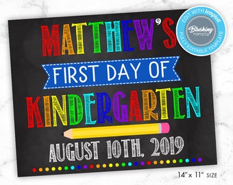May include: A chalkboard sign with the text "MATTHEW'S FIRST DAY OF KINDERGARTEN AUGUST 10TH, 2019" in rainbow colors. The sign is 14 inches by 11 inches.