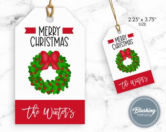 Puede incluir: Una etiqueta de regalo blanca con un diseño de corona navideña roja y verde. La etiqueta tiene el texto "Merry Christmas" y "The Winter's" en letras negras. La etiqueta mide 2,25 pulgadas por 3,75 pulgadas.