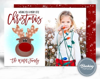 May include: A Christmas card featuring a cartoon reindeer with a red nose and a blue background. The card says "Wishing you a merry little Christmas" and "The Winter Family". A photo of a young girl holding Christmas lights is in the background.
