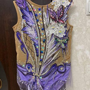 Puede incluir: Un leotardo morado y marrón con un diseño de mariposa y flores. El leotardo está decorado con pedrería y lentejuelas.