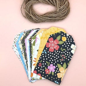 May include: A set of colorful patterned gift tags with a roll of twine. The tags are made of paper and have a variety of floral designs. The twine is brown and natural.
