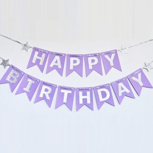 May include: A lavender banner with silver glitter lettering that reads "HAPPY BIRTHDAY". The banner is strung on a silver cord and has silver star accents. Perfect for birthday celebrations.