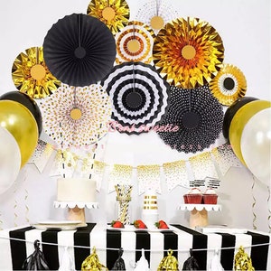 May include: A festive party scene with black, gold, and white decorations. Includes paper fans, balloons, a banner, and a table with a cake, cupcakes, and strawberries. The table has a black and white striped tablecloth.