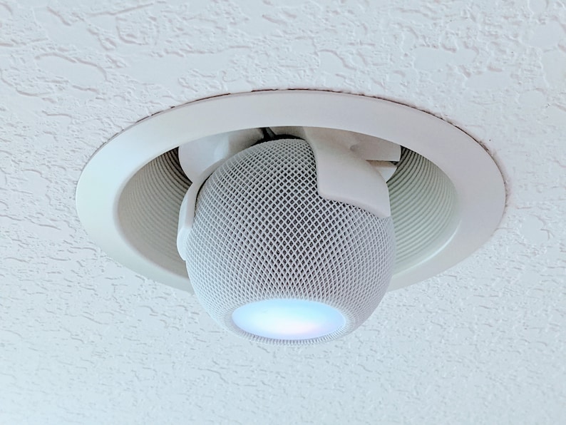 May include: A white smart speaker with a mesh grille is mounted in a white ceiling fixture. The speaker is lit with a blue light.