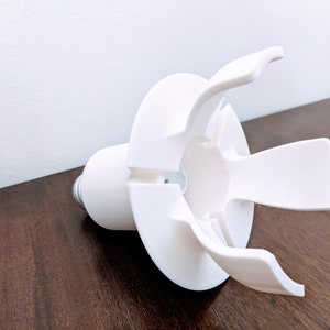 May include: White plastic light bulb holder with four prongs. The holder is designed to fit a standard light bulb.