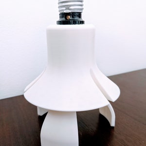 May include: White plastic light bulb adapter with a standard light bulb socket and three prongs for stability.