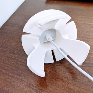 May include: White cable management organiser with six slots for cords. The organiser is designed to hold and organise cords and cables, keeping them tidy and out of sight.