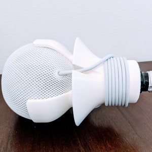 May include: White 3D printed light bulb socket adapter with a white cord wrapped around it. The adapter is designed to fit a smart speaker.