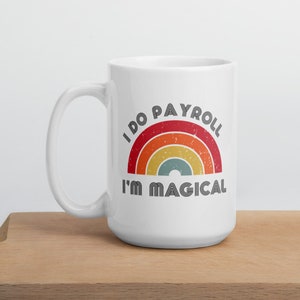 May include: White ceramic mug with a handle, featuring a retro rainbow design and the text "I DO PAYROLL I'M MAGICAL" in black. The mug is placed on a wooden cutting board.
