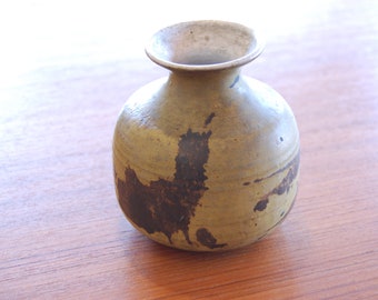 May include: A small, round, ceramic vase with a brown and yellow glaze. The vase has a wide mouth and a narrow neck.