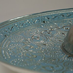 May include: A silver serving tray with a blue, embossed design. The tray has a raised centre section and a decorative border.