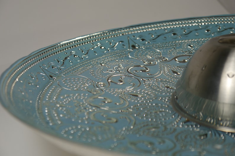 May include: A silver serving tray with a blue, embossed design. The tray has a raised centre section and a decorative border.