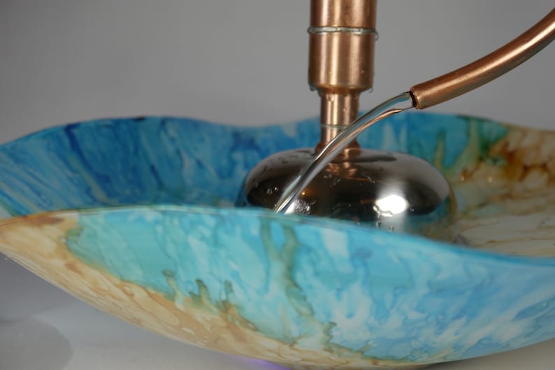 May include: A copper and stainless steel fountain with a blue and brown glass bowl. Water flows from a copper pipe into the bowl.