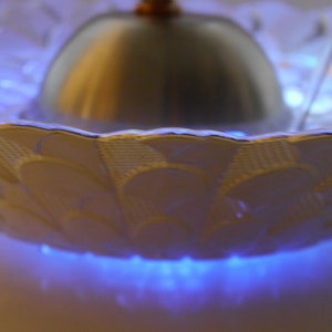 May include: A white ceramic fountain with a silver dome and blue LED lights. The fountain has a decorative pattern on the rim.
