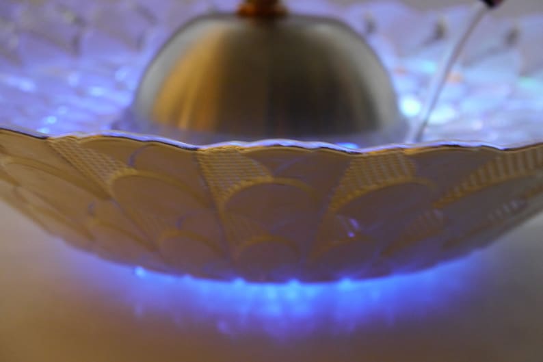 May include: A white ceramic fountain with a silver dome and blue LED lights. The fountain has a decorative pattern on the rim.