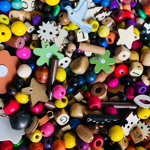 May include: A large collection of colorful wooden beads, shapes, and letters. The beads are in various colors, including red, blue, green, yellow, and brown. The shapes include stars, flowers, and birds. The letters are in various sizes and fonts.