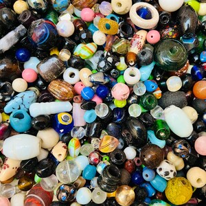 May include: A large assortment of colorful and patterned beads, including glass, wood, and stone beads. The beads are in various shapes and sizes, and some have intricate designs.