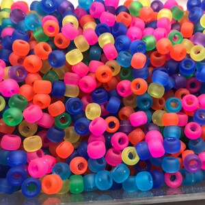 May include: A large pile of colorful translucent plastic beads. The beads are in various shades of blue, green, yellow, orange, pink, and purple.