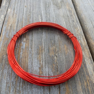May include: A coil of bright red wire, wound into a circle, on a wooden surface.