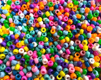 Puede incluir: Un gran surtido de cuentas de plástico de colores en varios tonos de azul, verde, rosa, morado, amarillo, naranja y blanco. Las cuentas son todas del mismo tamaño y forma, y están dispuestas en un patrón aleatorio.