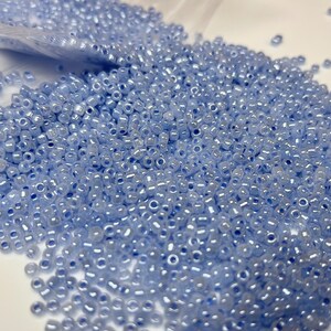 May include: A large quantity of small, light blue glass seed beads. The beads have a subtle iridescent sheen.
