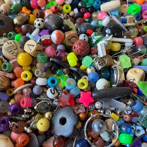 May include: A colorful assortment of beads and small decorative items. The collection includes various shapes, sizes, and colors, such as round, star, and cube-shaped beads. Materials include plastic, metal, and wood. The beads are in shades of red, yellow, green, blue, and purple.