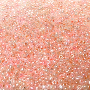 May include: A close-up view of a large quantity of small, round, iridescent pink beads. The beads have a translucent, glassy appearance.