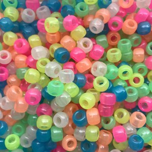 May include: A large pile of colorful glow-in-the-dark plastic beads. The beads are round and have a hole in the center. The colors include pink, green, blue, yellow, and white.