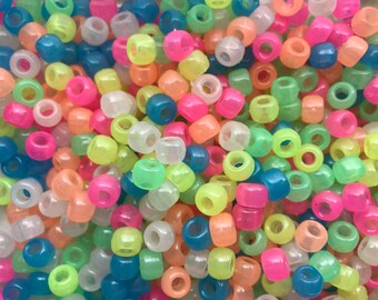 May include: A large pile of colorful glow-in-the-dark plastic beads. The beads are round and have a hole in the center. The colors include pink, green, blue, yellow, and white.