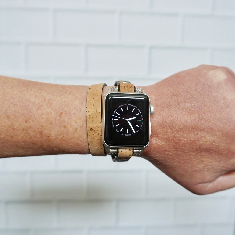 May include: A silver Apple Watch with a black face and a brown cork band. The watch is worn on a person's wrist.
