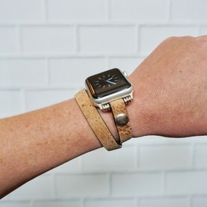 May include: A tan cork band watch strap with a silver Apple Watch on a person's wrist.